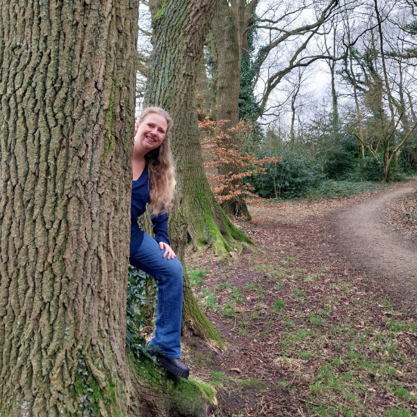 Pauline de Vries kijkt om een boom heen.